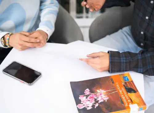 Dos personas conversando frente a frente; sobre la mesa hay un libro y un teléfono.