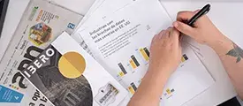 Persona con un bolígrafo en la mano, y varios libros sobre la mesa.